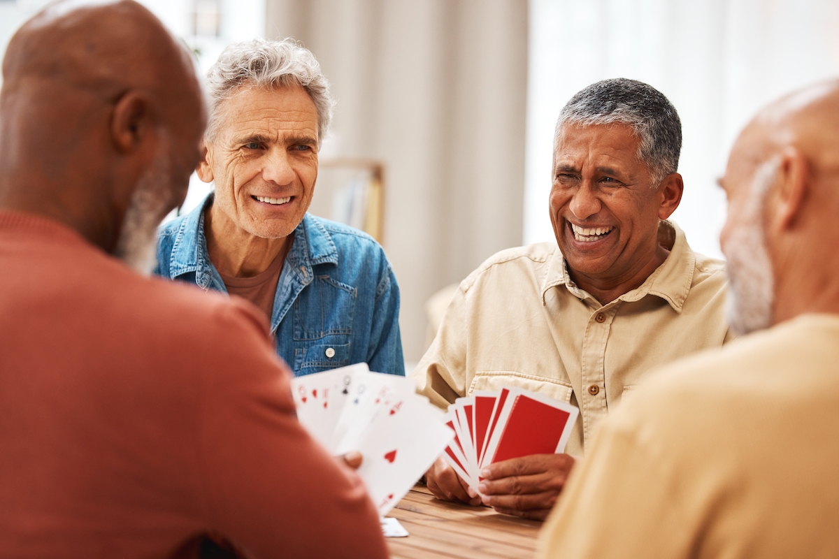 Senior man, friends and laughing for card games on wooden table in fun activity, social bonding or gathering. Group of happy elderly men with cards for poker game enjoying play time together at home